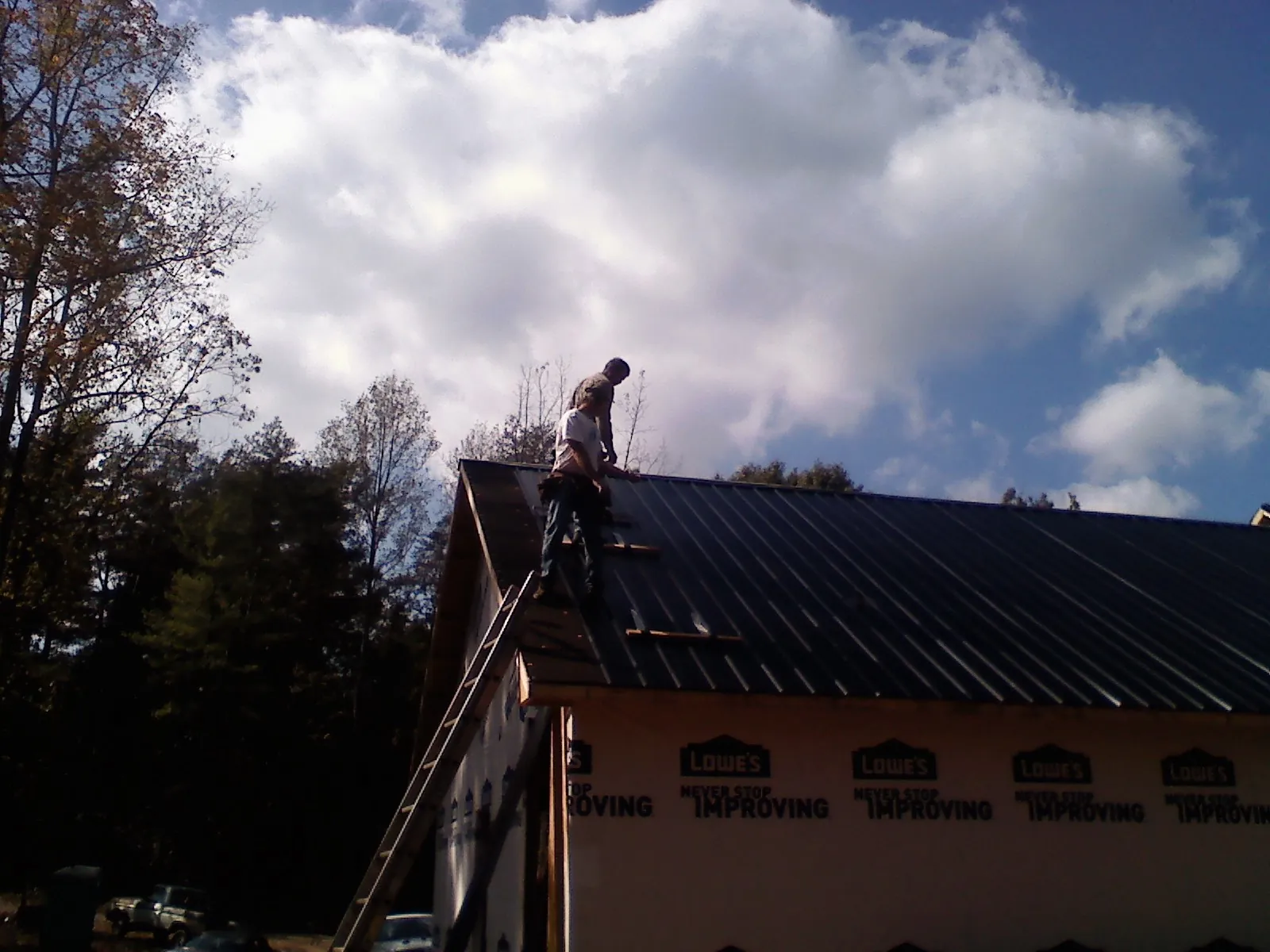 Roofer fastening dark metal panels high against a cloudy sky, from a Roof Inspection job in New River