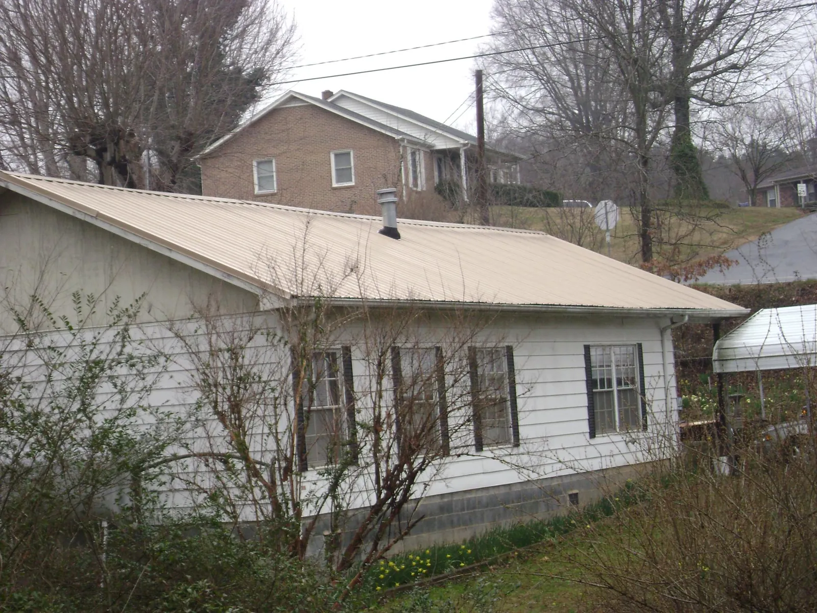 Tan metal roof on a white sided house set into a hillside — Commercial Roofing by Roofing Brothers in New River
