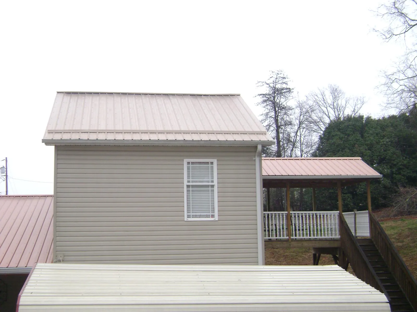 Tan metal roofs on a two story addition and attached porch, from a Roof Replacement job in New River